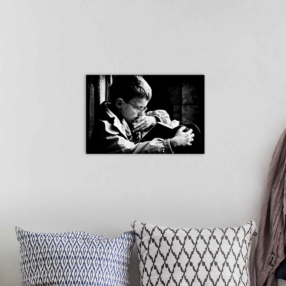A bohemian room featuring A young boy with glasses reads a book on his lap, Belgium.