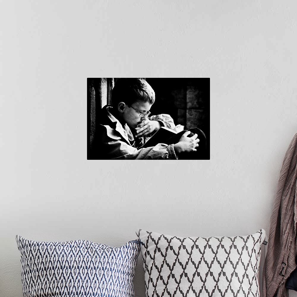 A bohemian room featuring A young boy with glasses reads a book on his lap, Belgium.