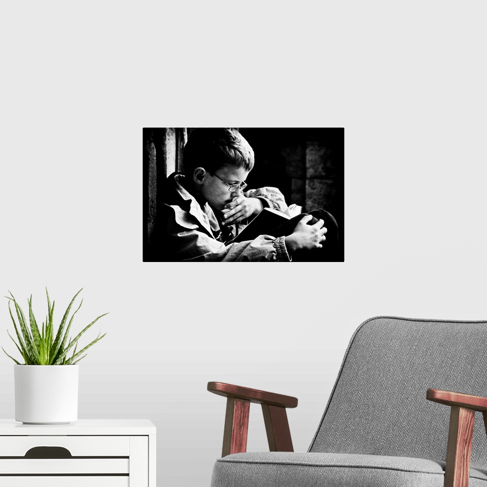 A modern room featuring A young boy with glasses reads a book on his lap, Belgium.