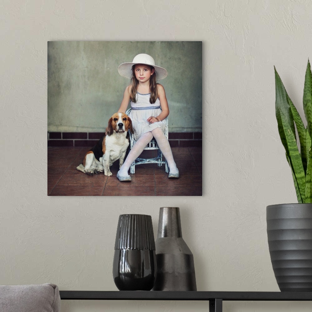 A modern room featuring A young girl in a dress and hat sitting on a chair with her pet beagle.