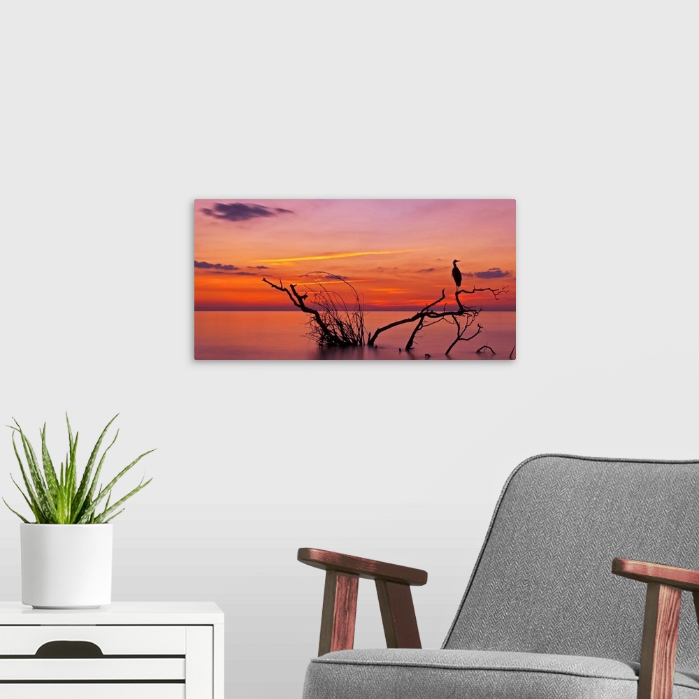 A modern room featuring Landscape photograph of a beautiful orange, red, yellow, purple and pink sunset over calm water.