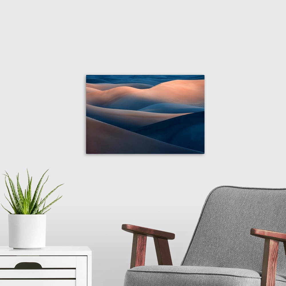 A modern room featuring A desert landscape with tall blue and orange sand dunes in the evening.