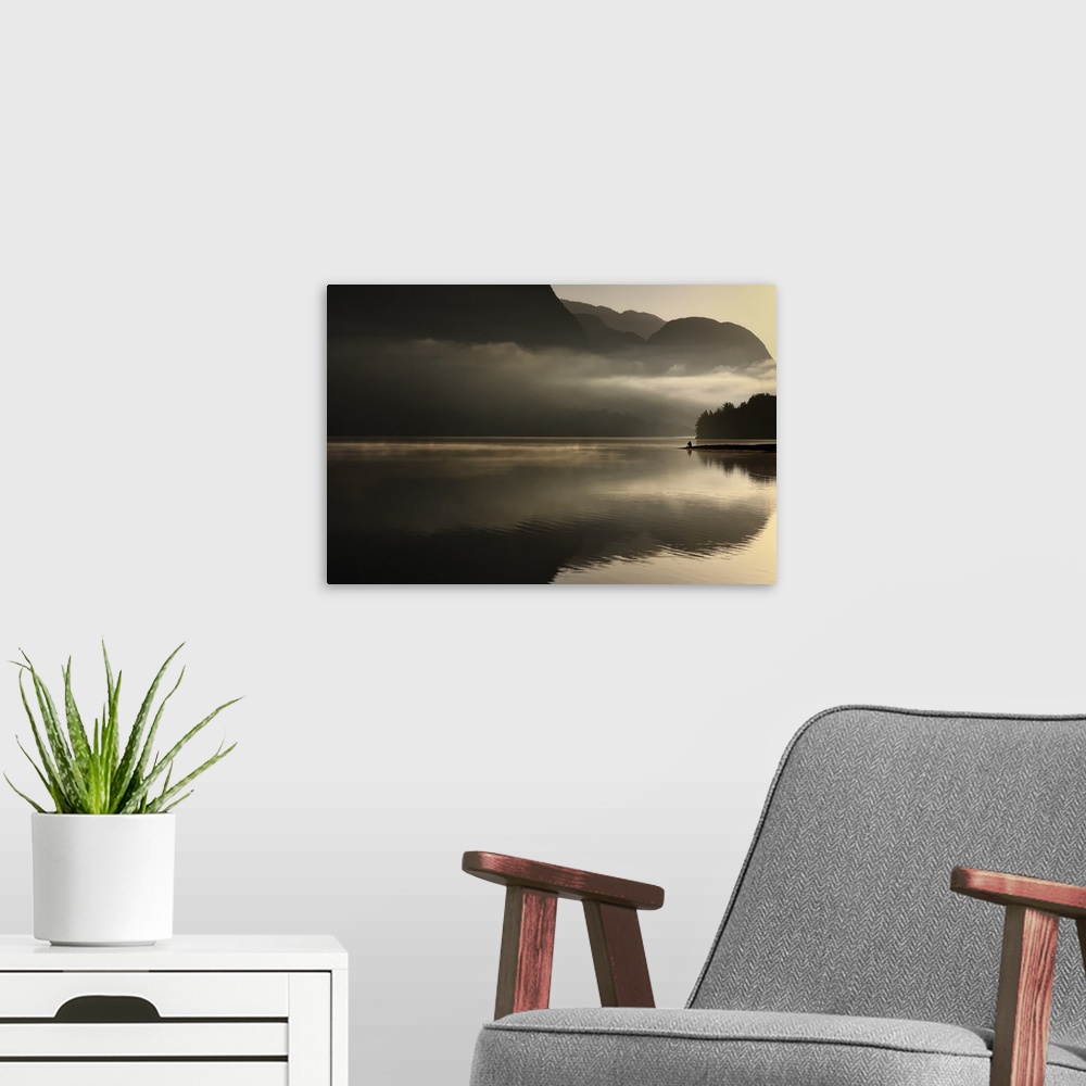 A modern room featuring Distant figure sitting on the banks of a lake with misty clouds at sunset.