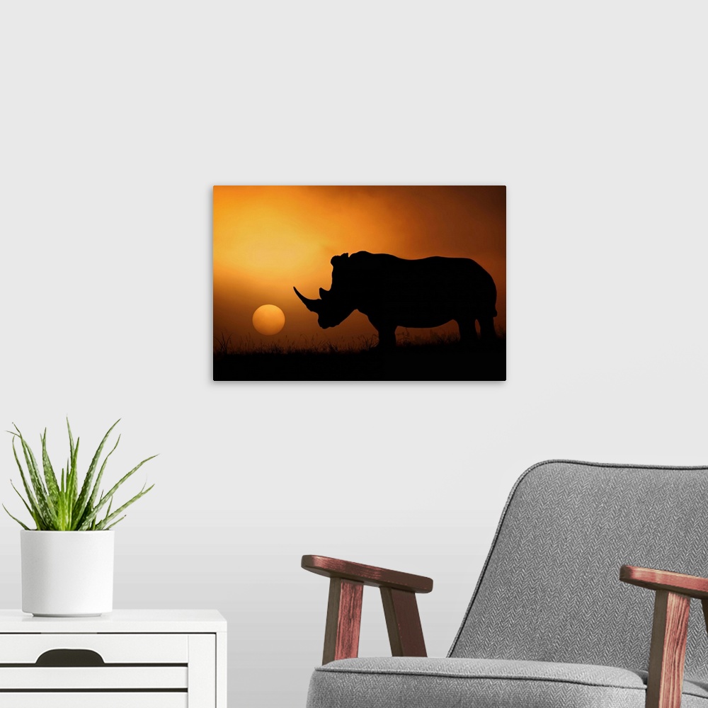 A modern room featuring A rhinoceros stands in silhouette in the African Savannah with the sun setting in the distance.