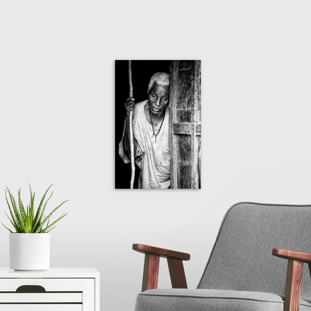 A modern room featuring Black and white portrait of an elderly person with a staff in a doorway.