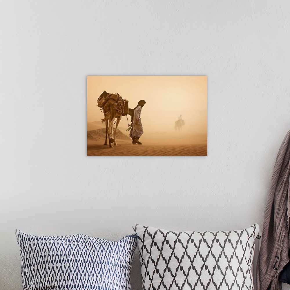A bohemian room featuring A man walks a camel carrying bags through a sandstorm in the desert in Morocco.