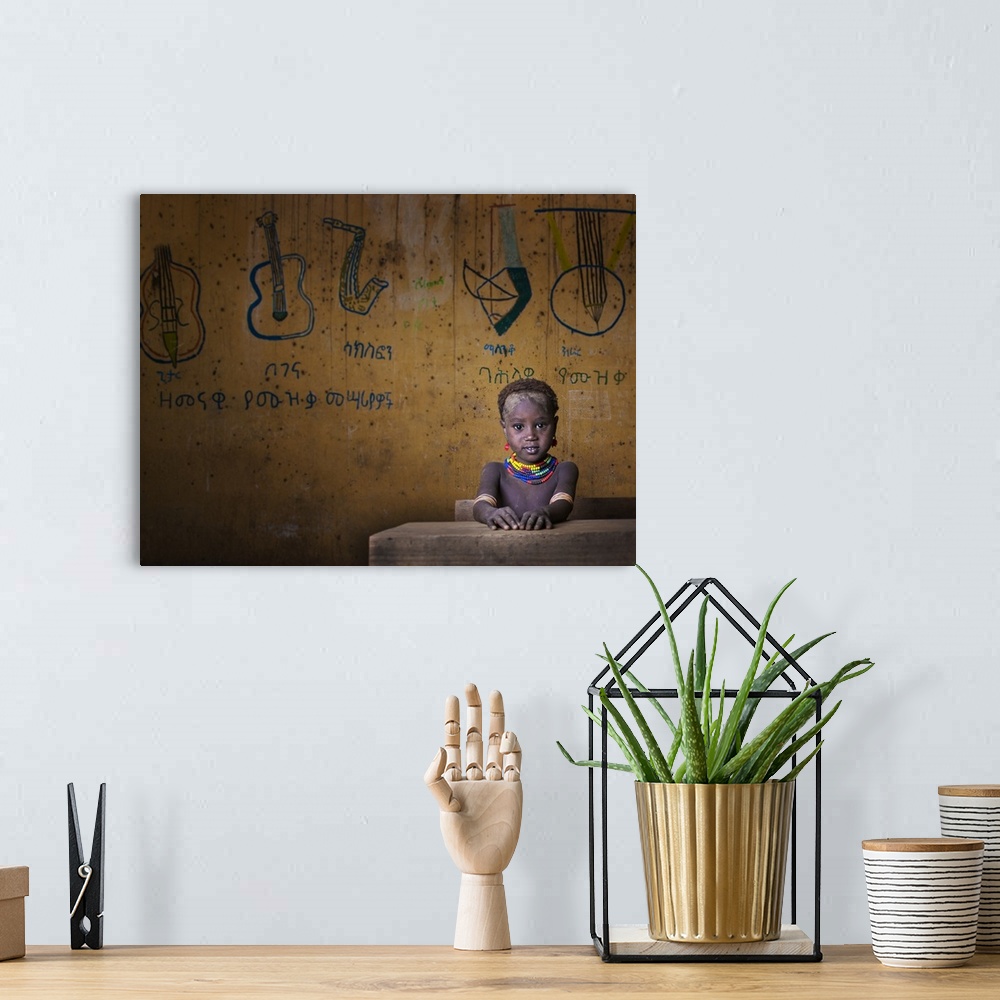 A bohemian room featuring Portrait of a young child wearing a beaded necklace seated at a desk with drawings of musical ins...