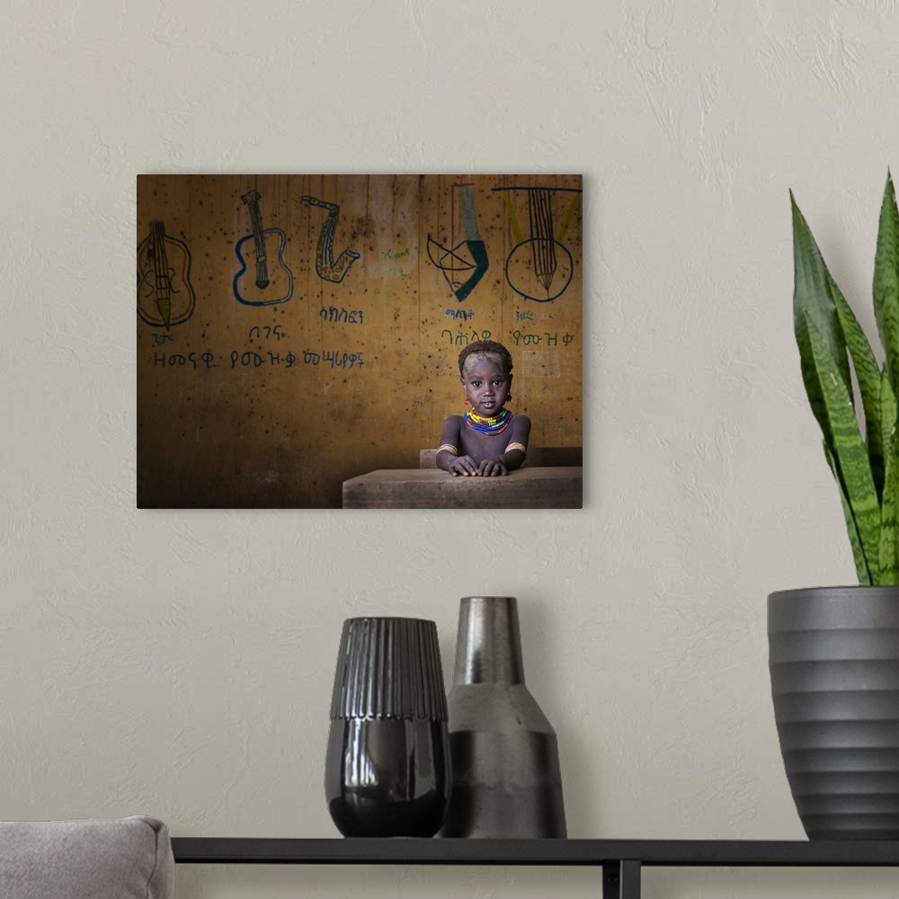 A modern room featuring Portrait of a young child wearing a beaded necklace seated at a desk with drawings of musical ins...