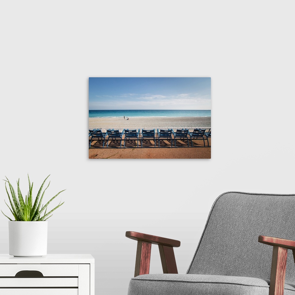 A modern room featuring Landscape photograph of the ocean shore with a row of blue beach chairs.