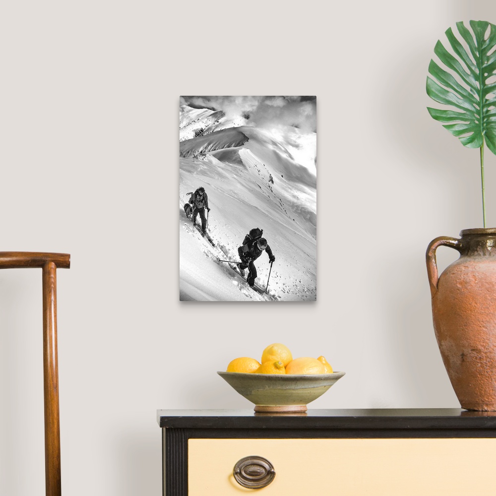 A traditional room featuring Two people and a dog trek through the snow on an alpine mountaintop.