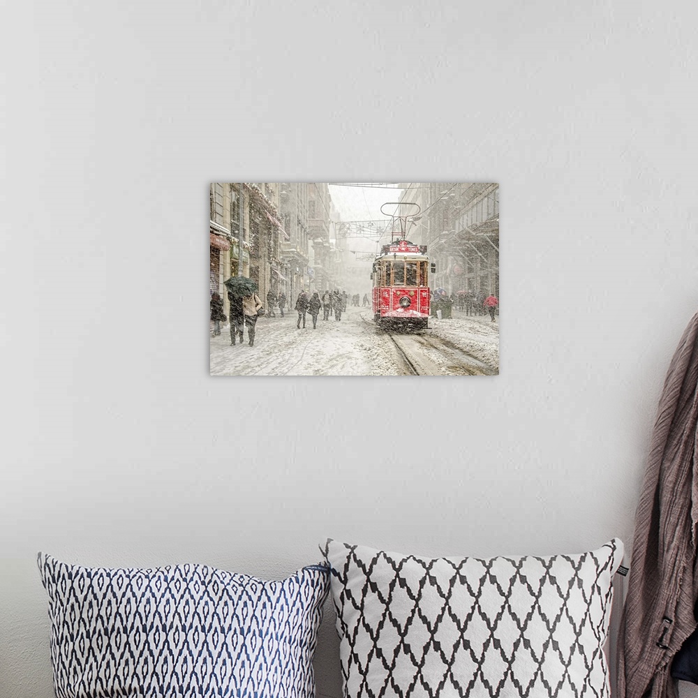 A bohemian room featuring A snowstorm raining down on a city with a red street car in the street.