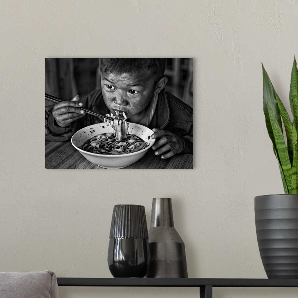 A modern room featuring A young boy eats a bowl of noodles with chopsticks.