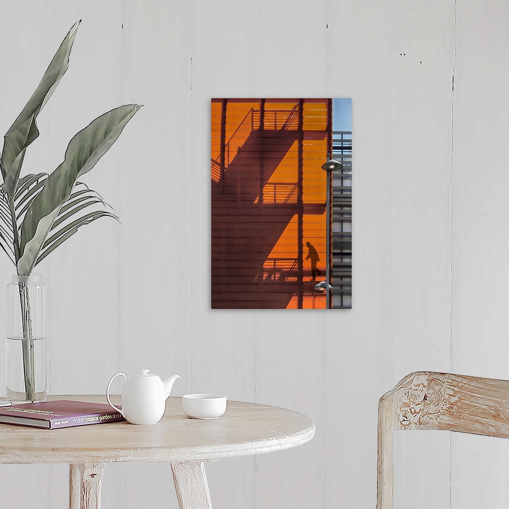 A farmhouse room featuring Shadow of a fire escape staircase and a person walking down cast onto the side of an orange build...