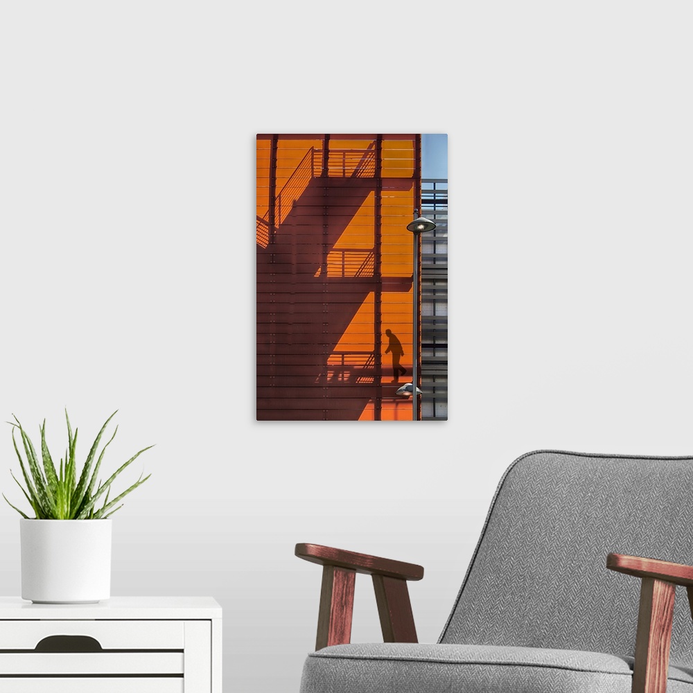 A modern room featuring Shadow of a fire escape staircase and a person walking down cast onto the side of an orange build...