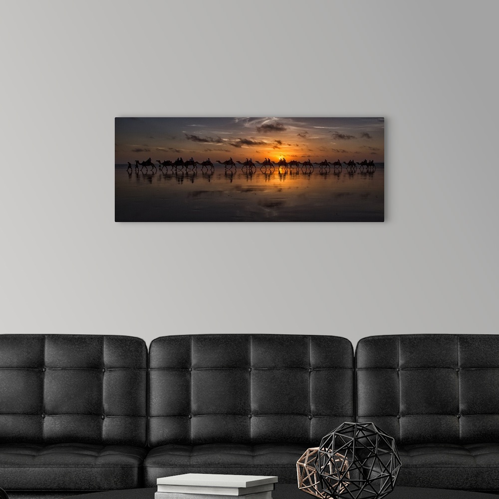 A modern room featuring Panoramic photograph of a line of camels walking through the desert at sunset.