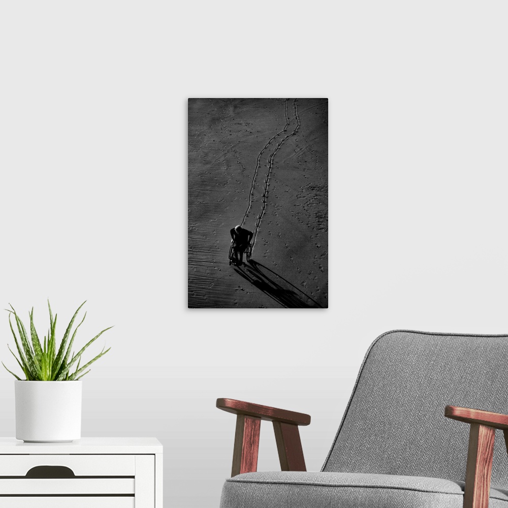 A modern room featuring Black and white photograph of a person using their wheel chair in the sand, leaving a lined trail...