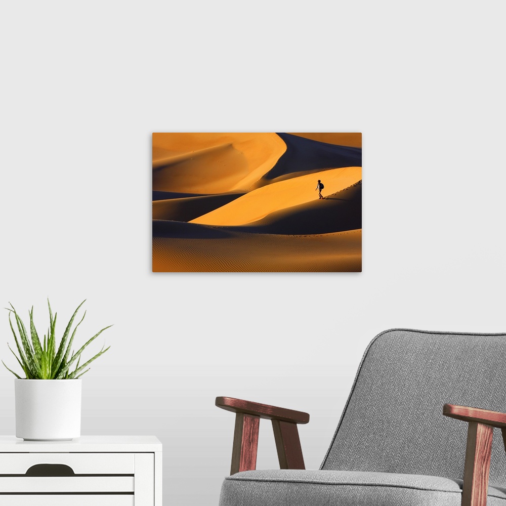 A modern room featuring A person walks on a sand dune in a golden desert at sunset.