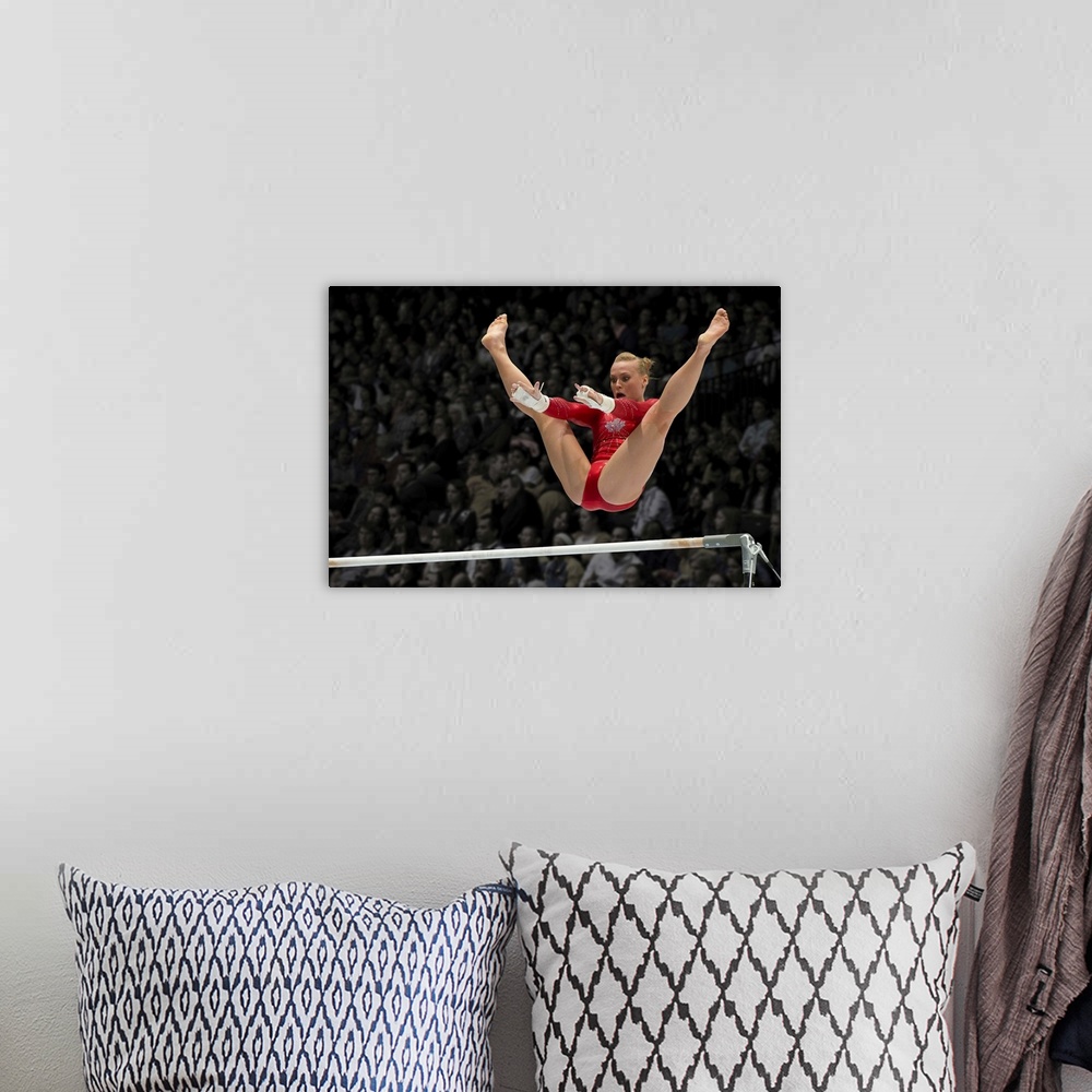 A bohemian room featuring A female gymnast flies over the high bar with her legs raised up, arms outstretched ready to grab...