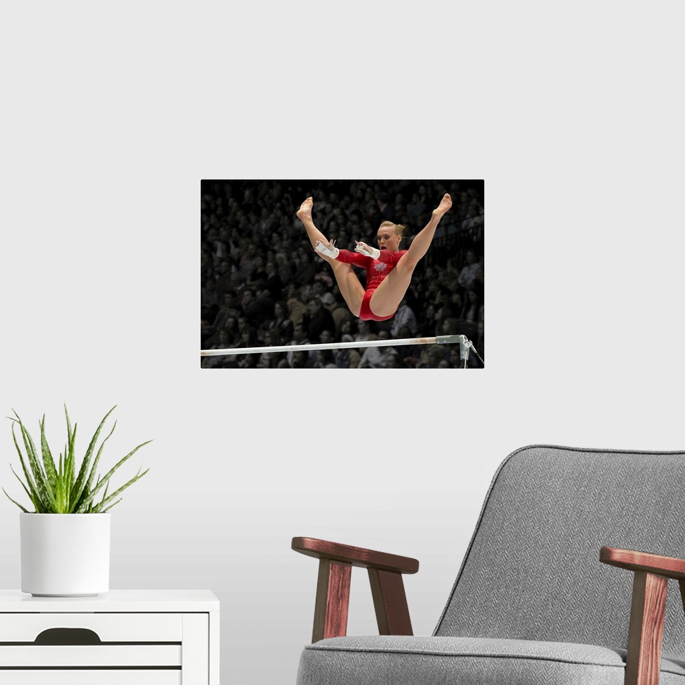 A modern room featuring A female gymnast flies over the high bar with her legs raised up, arms outstretched ready to grab...