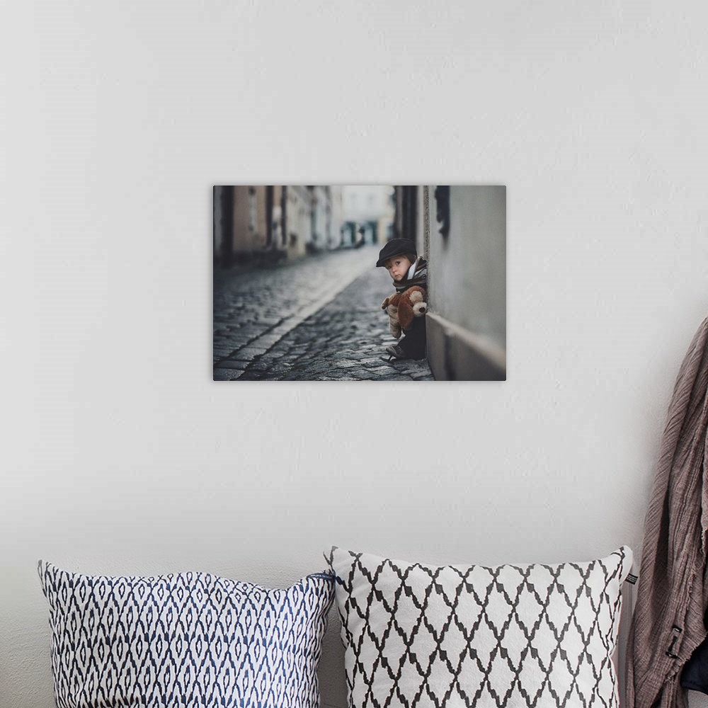 A bohemian room featuring A portrait of a little boy sitting on a doorstep on a cobblestone road.