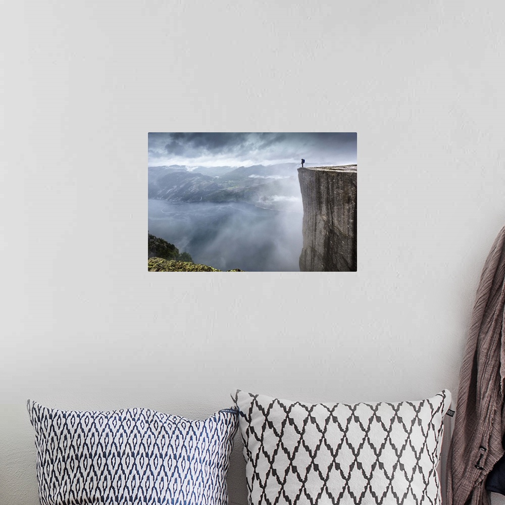 A bohemian room featuring A hiker stands at the edge of a steep cliff overlooking a misty fjord, Prekestolen, Norway.
