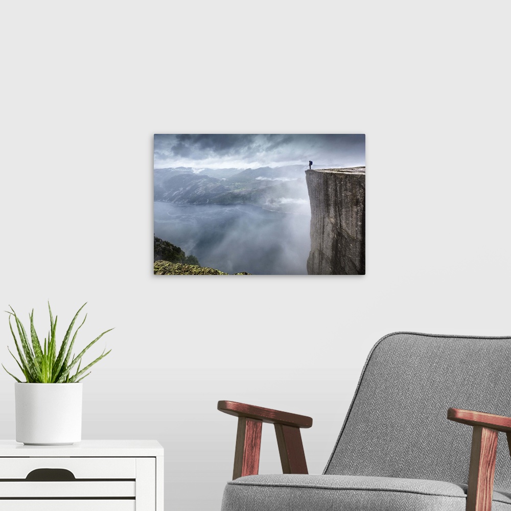 A modern room featuring A hiker stands at the edge of a steep cliff overlooking a misty fjord, Prekestolen, Norway.