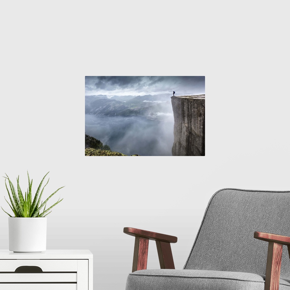 A modern room featuring A hiker stands at the edge of a steep cliff overlooking a misty fjord, Prekestolen, Norway.