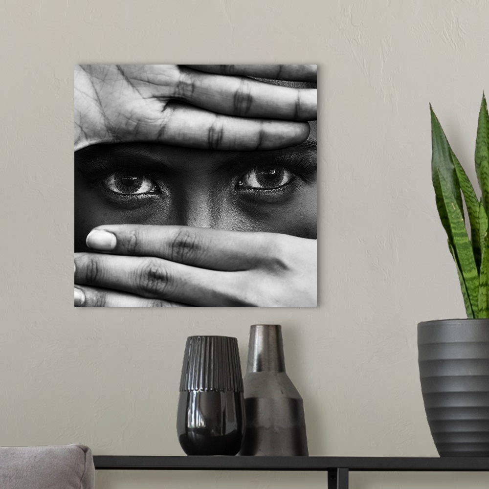 A modern room featuring A black and white portrait of a close-up of hands covering a persons leaving the eyes exposed.