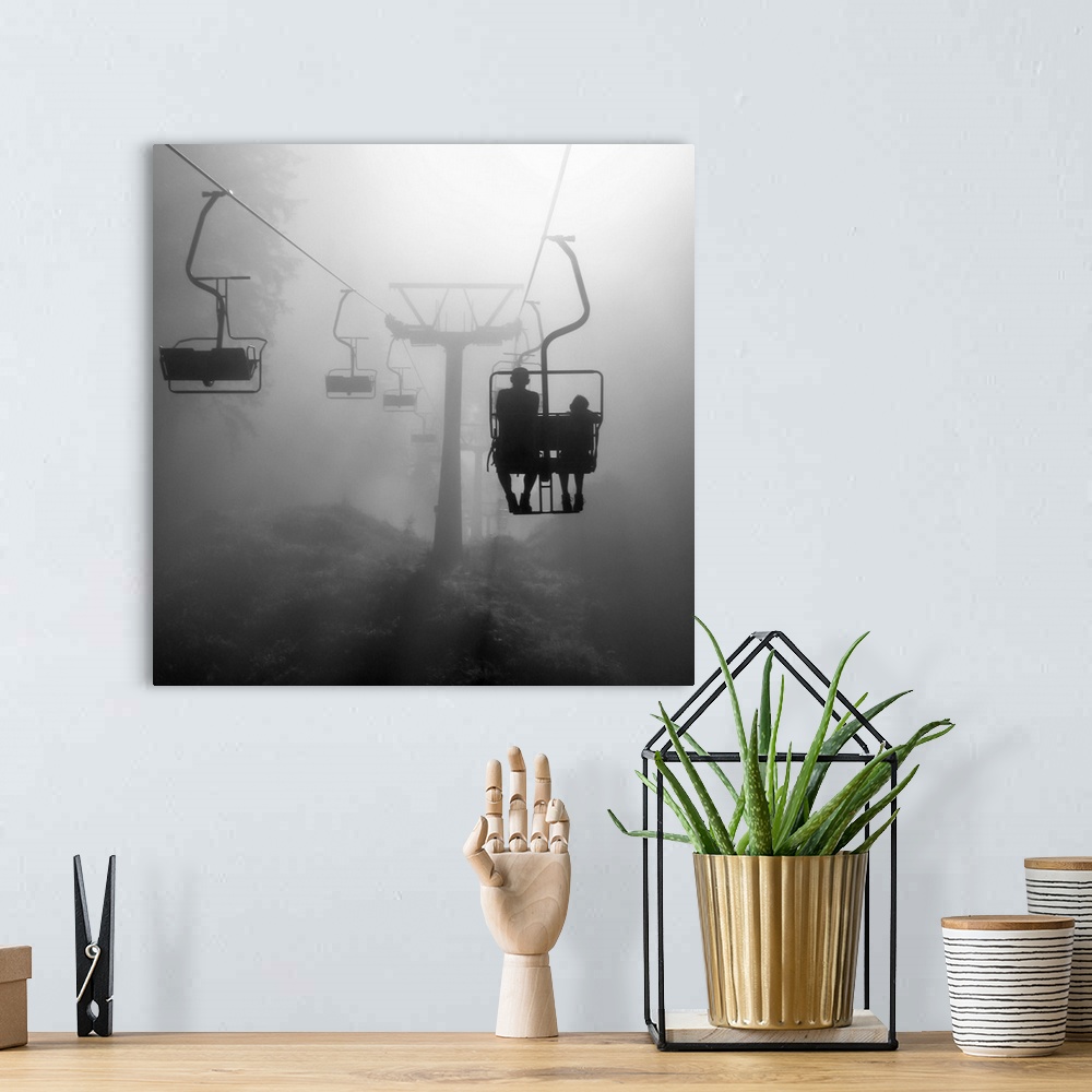 A bohemian room featuring Two silhouetted people on a chairlift heading into the dense fog.