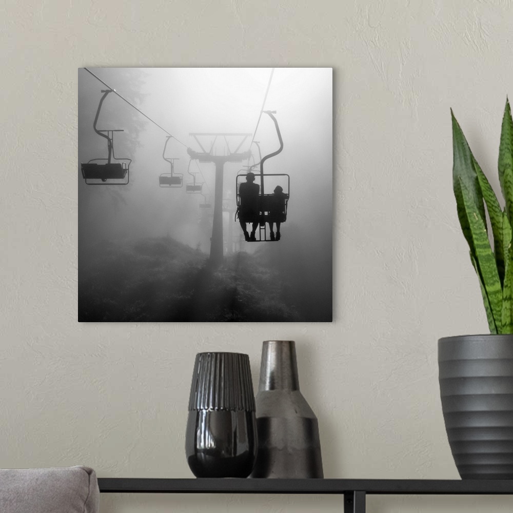 A modern room featuring Two silhouetted people on a chairlift heading into the dense fog.