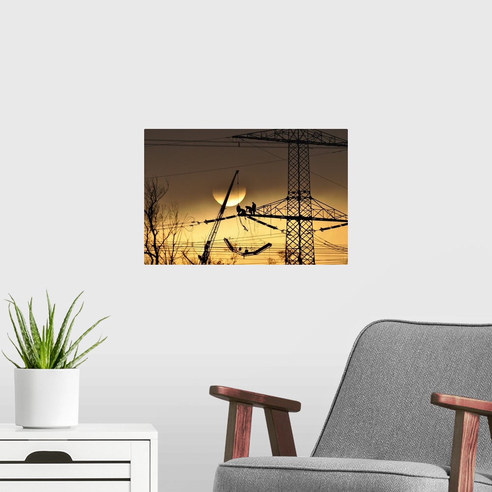 A modern room featuring Silhouette of people working on a large electrical pylon with the sun setting in the background.