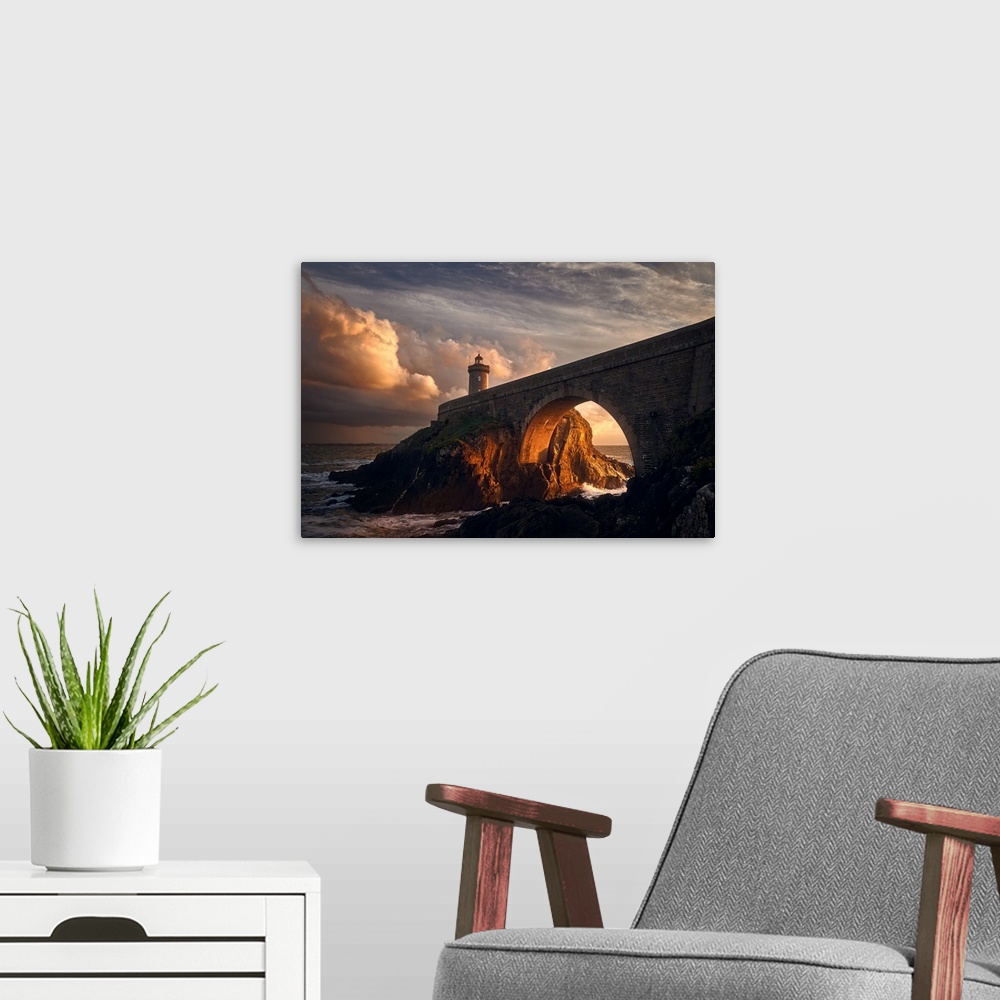 A modern room featuring Warm photograph of a rocky bridge over the ocean with an orange sunlit tunnel and a lighthouse on...