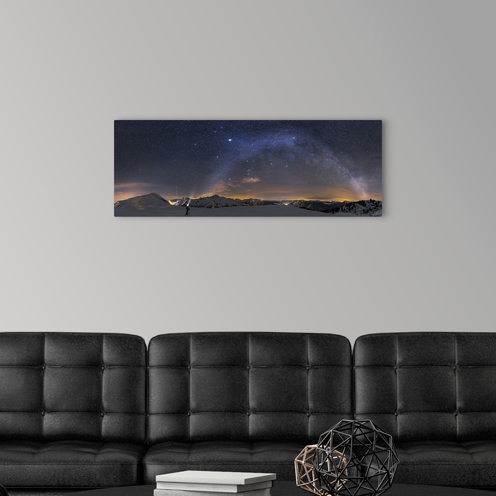 A modern room featuring A panoramic photograph of a person standing in a desolate mountainous snowscape under a starry ni...