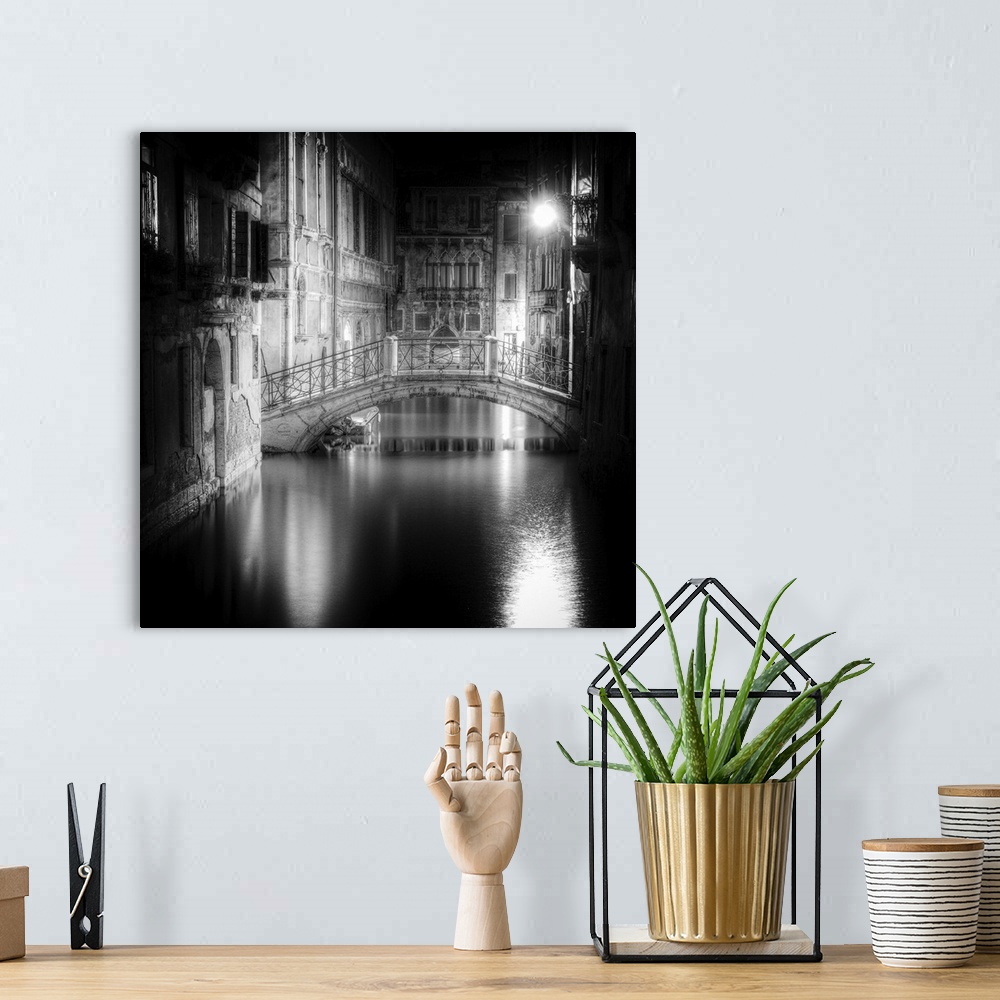 A bohemian room featuring High contrast black and white image of a bridge in a canal in the center of a city at night.