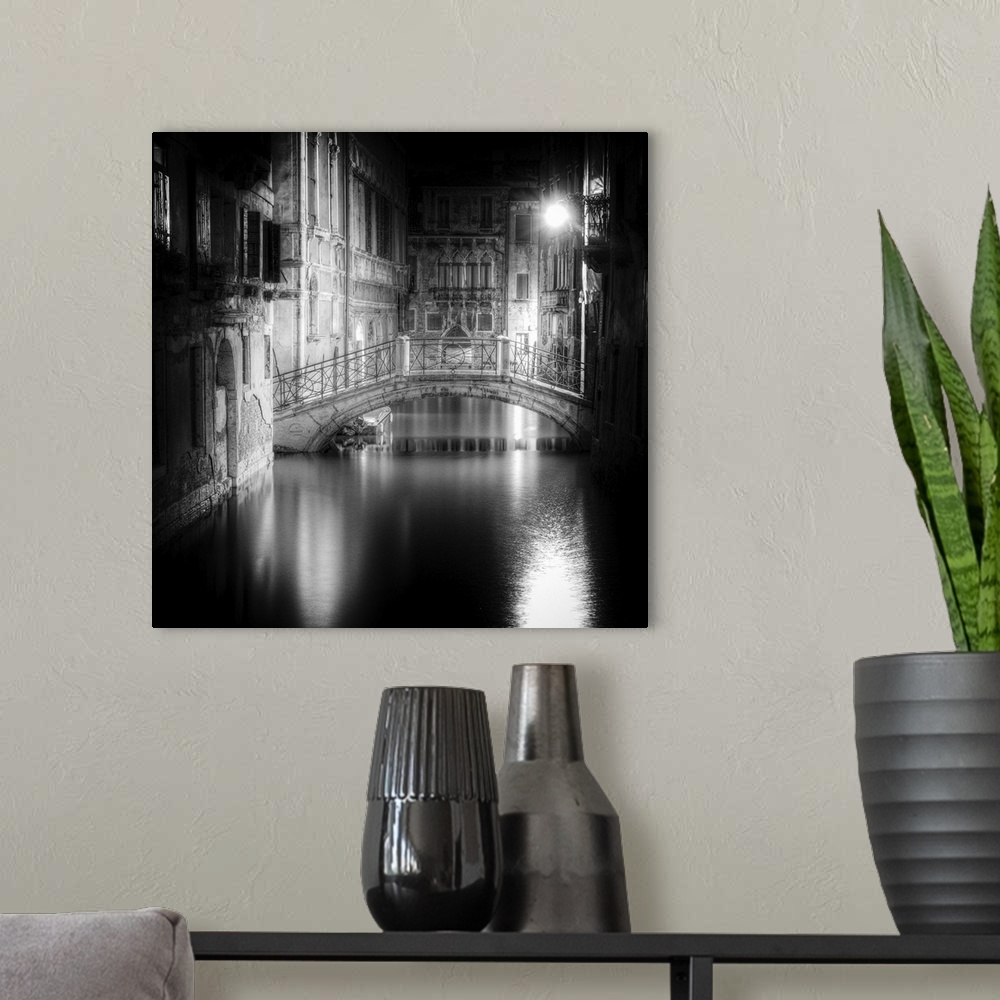 A modern room featuring High contrast black and white image of a bridge in a canal in the center of a city at night.