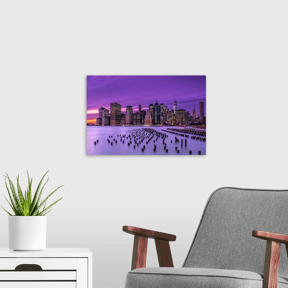 A modern room featuring Manhattan skyline at sunset under a purple sky, seen from Brooklyn.
