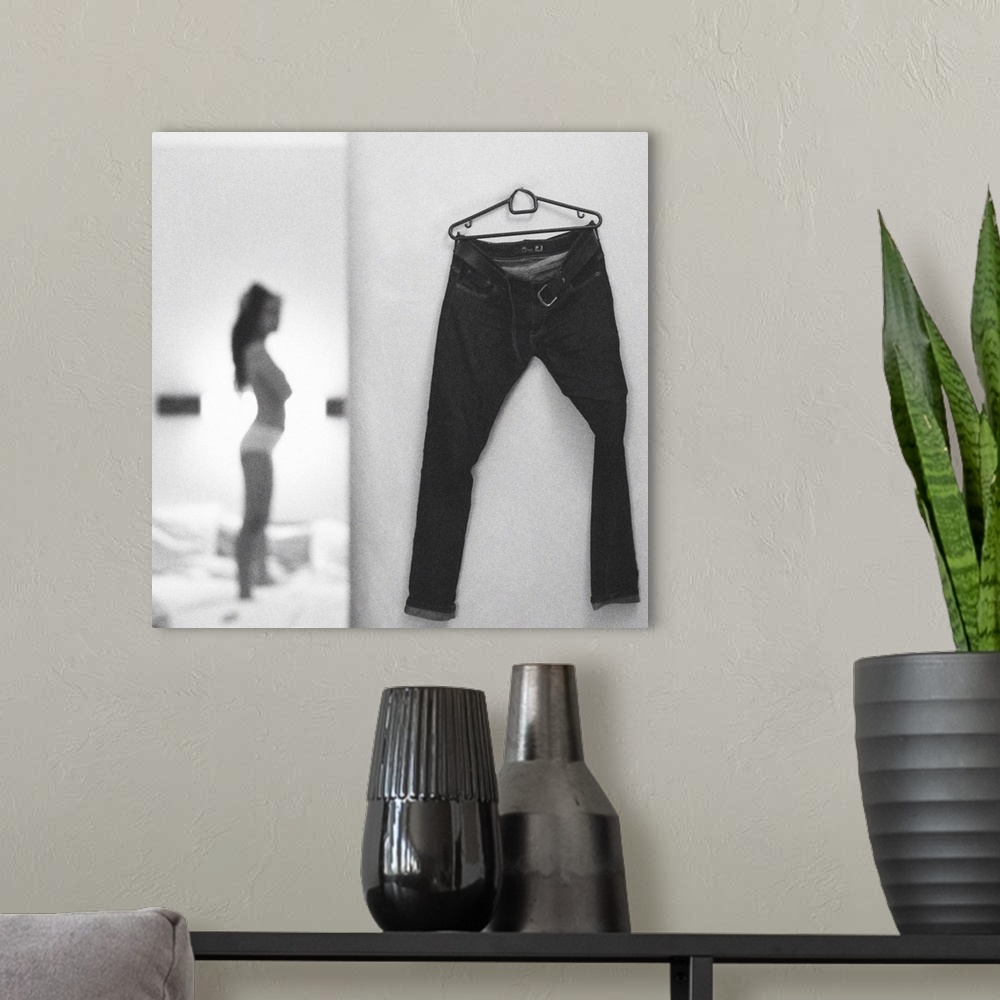 A modern room featuring A focus on a pair of pants hanging on a wall while a young woman in the background gets ready to ...
