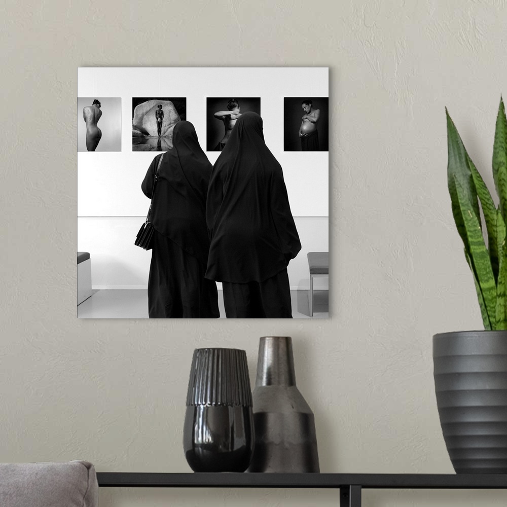 A modern room featuring Two women wearing veils looking at fine art in a museum.