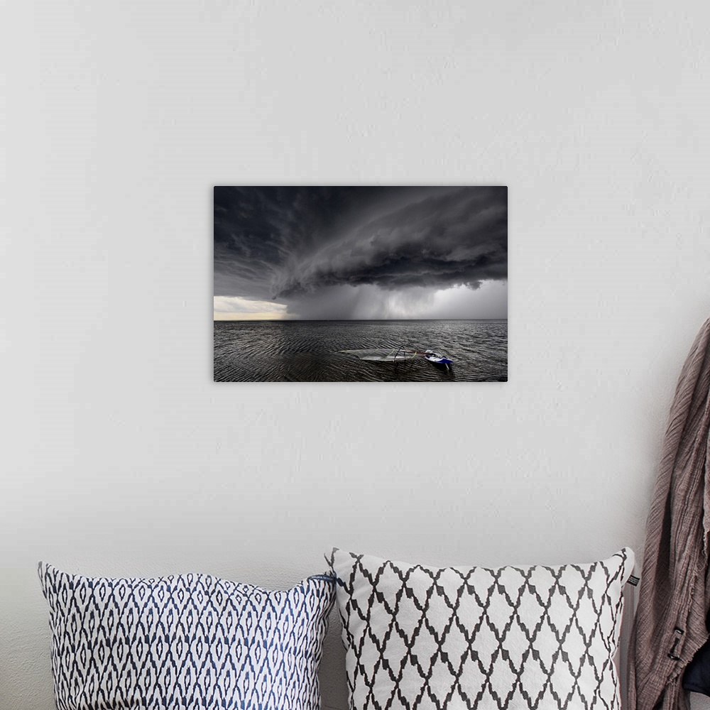 A bohemian room featuring A windsurfing board lays flat in the water as stormclouds with heavy rain approach.