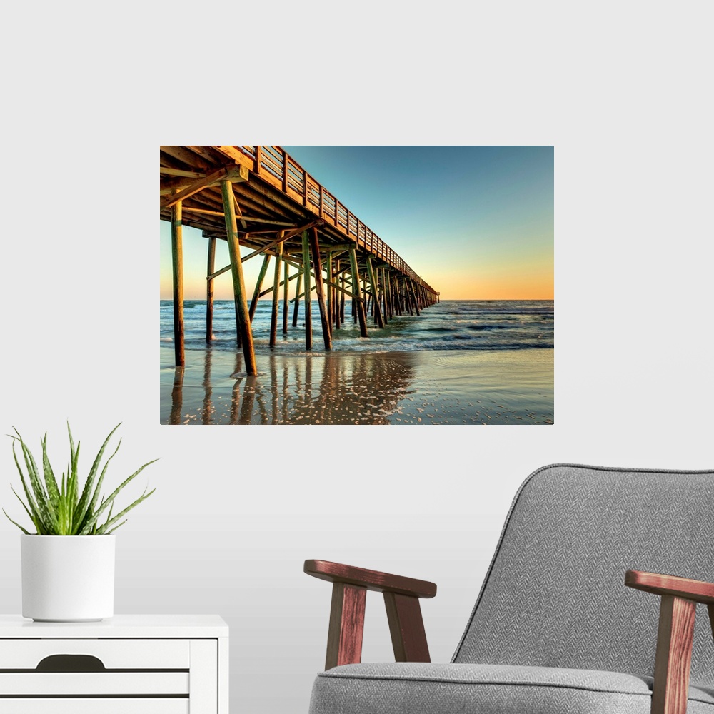 A modern room featuring A photograph of a long pier jetting out over the ocean. Sunlight glowing over the horizon as the ...