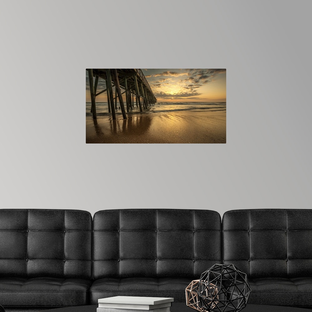 A modern room featuring A photograph of a long pier jetting out over the ocean. Sunlight bathing the sky in an orange glo...