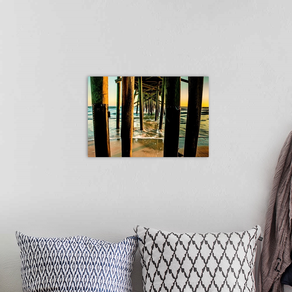 A bohemian room featuring A photograph looking through the underside of a long pier out over the ocean. The sky glowing wit...