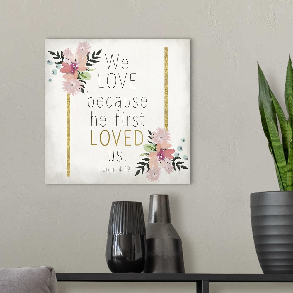 A modern room featuring Bible verse 1 John 4:19 with gold stripes and pink flowers.