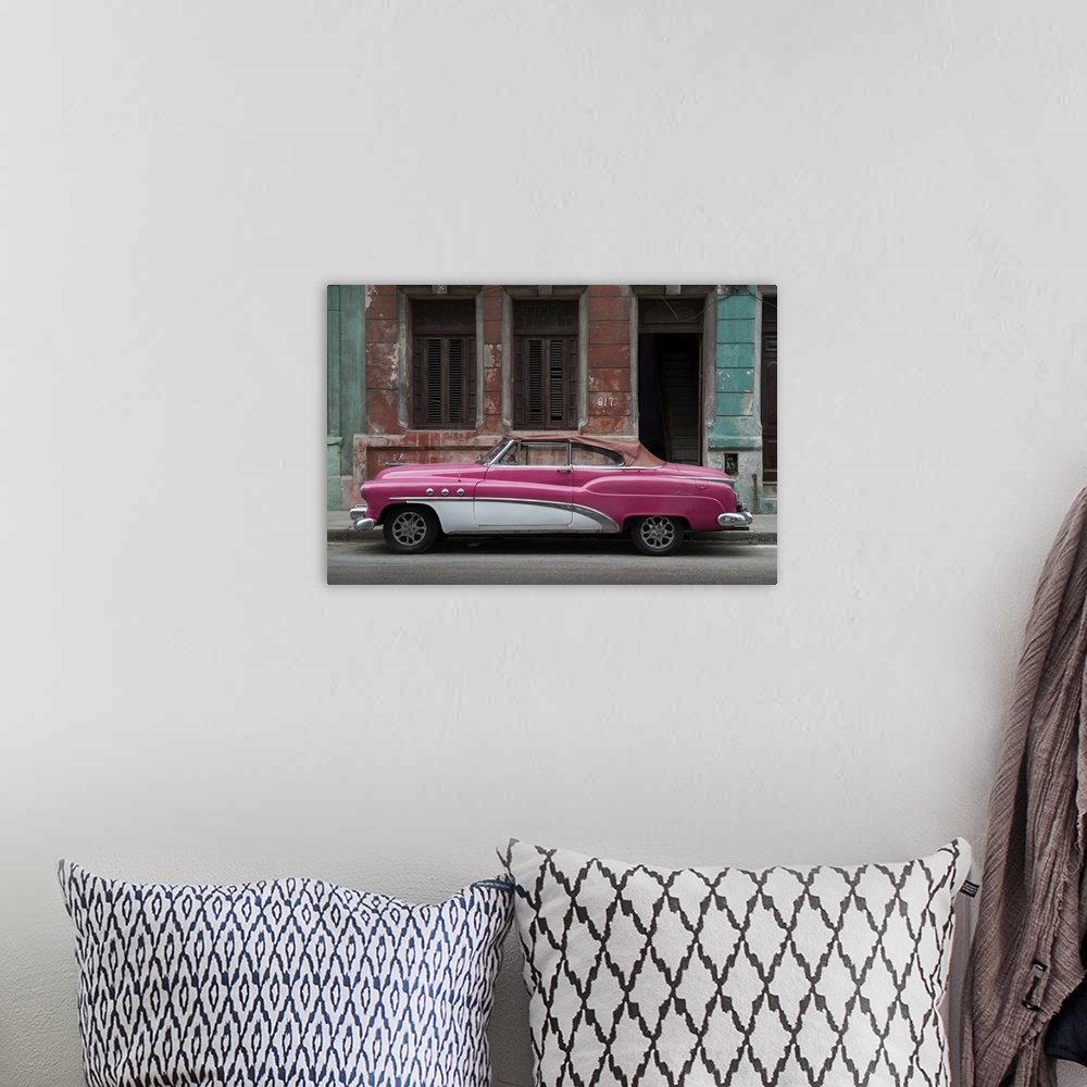A bohemian room featuring 1950s classic American pink car set against a traditional Cuban house.