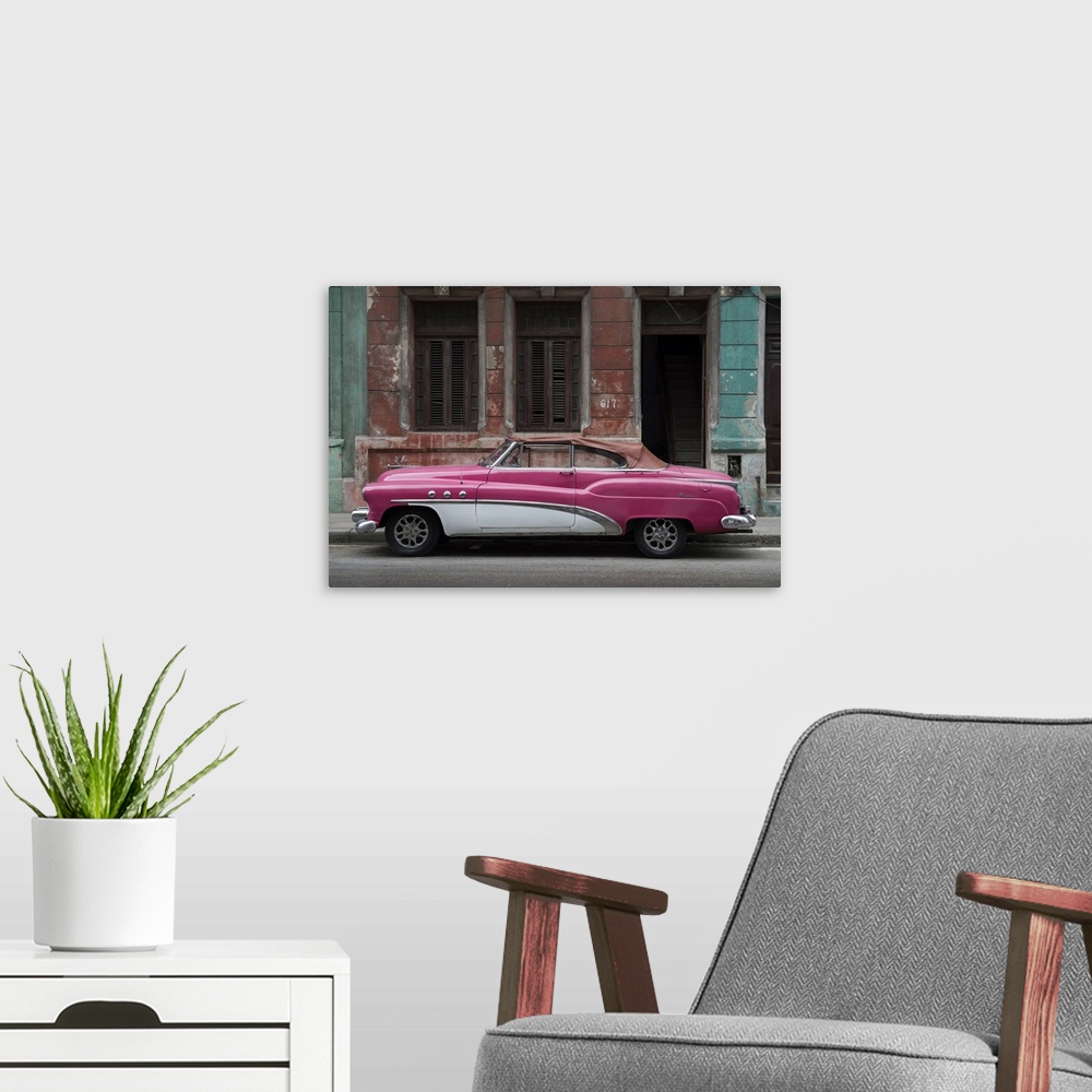 A modern room featuring 1950s classic American pink car set against a traditional Cuban house.