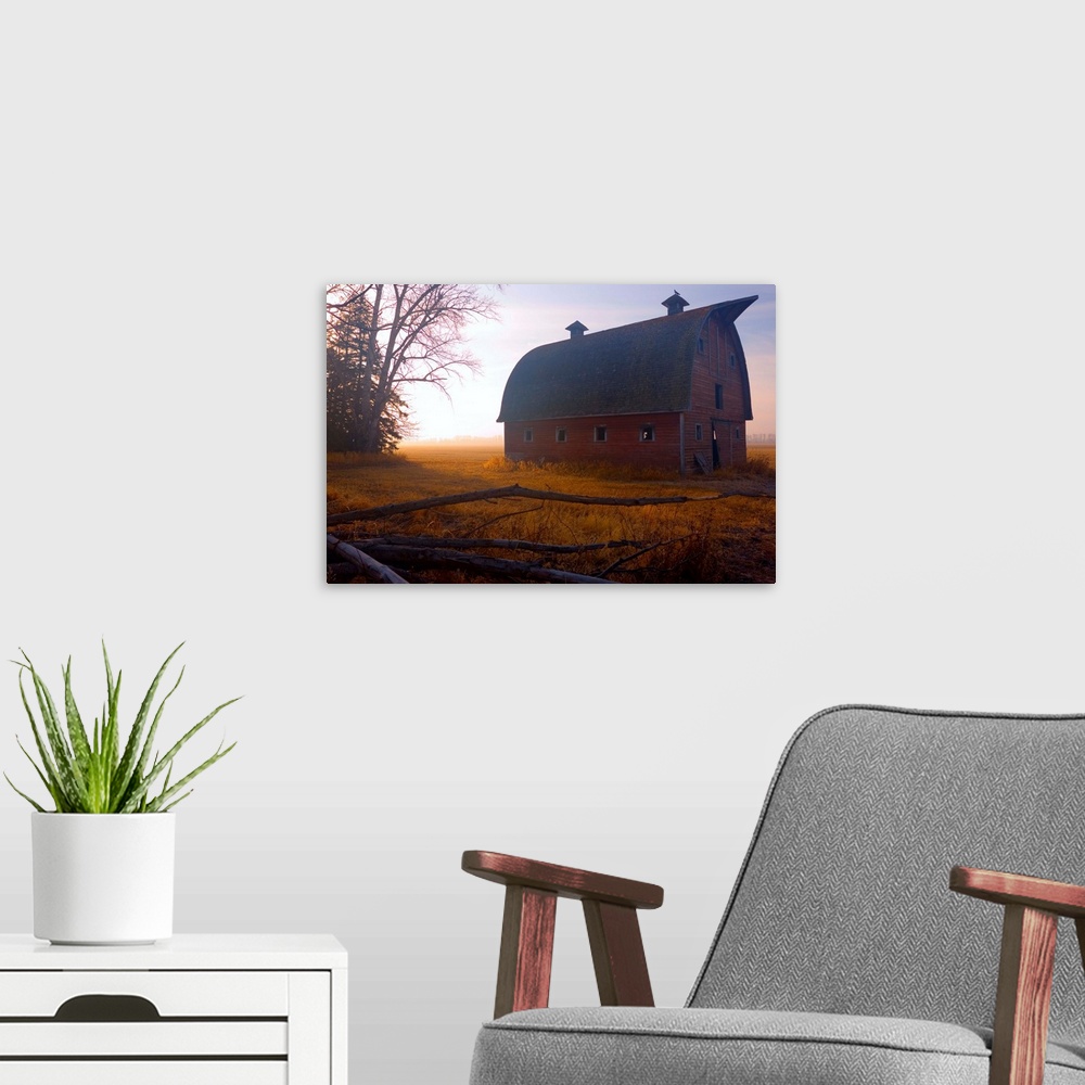 A modern room featuring A large barn is photographed in the morning during sunrise and there is a thin layer of fog over ...