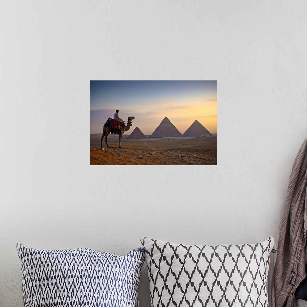 A bohemian room featuring A lone camel and rider stand in front of the setting sun with the great pyramids behind them; Giz...
