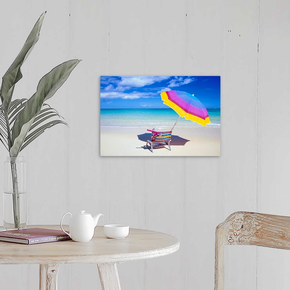 A farmhouse room featuring A large photograph of a colorful beach chair and umbrella sitting solely on the sand close to the...