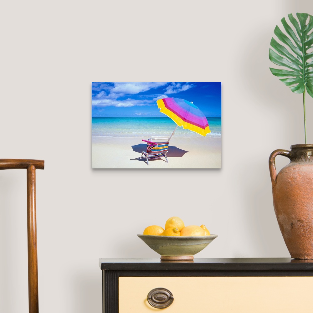 A traditional room featuring A large photograph of a colorful beach chair and umbrella sitting solely on the sand close to the...