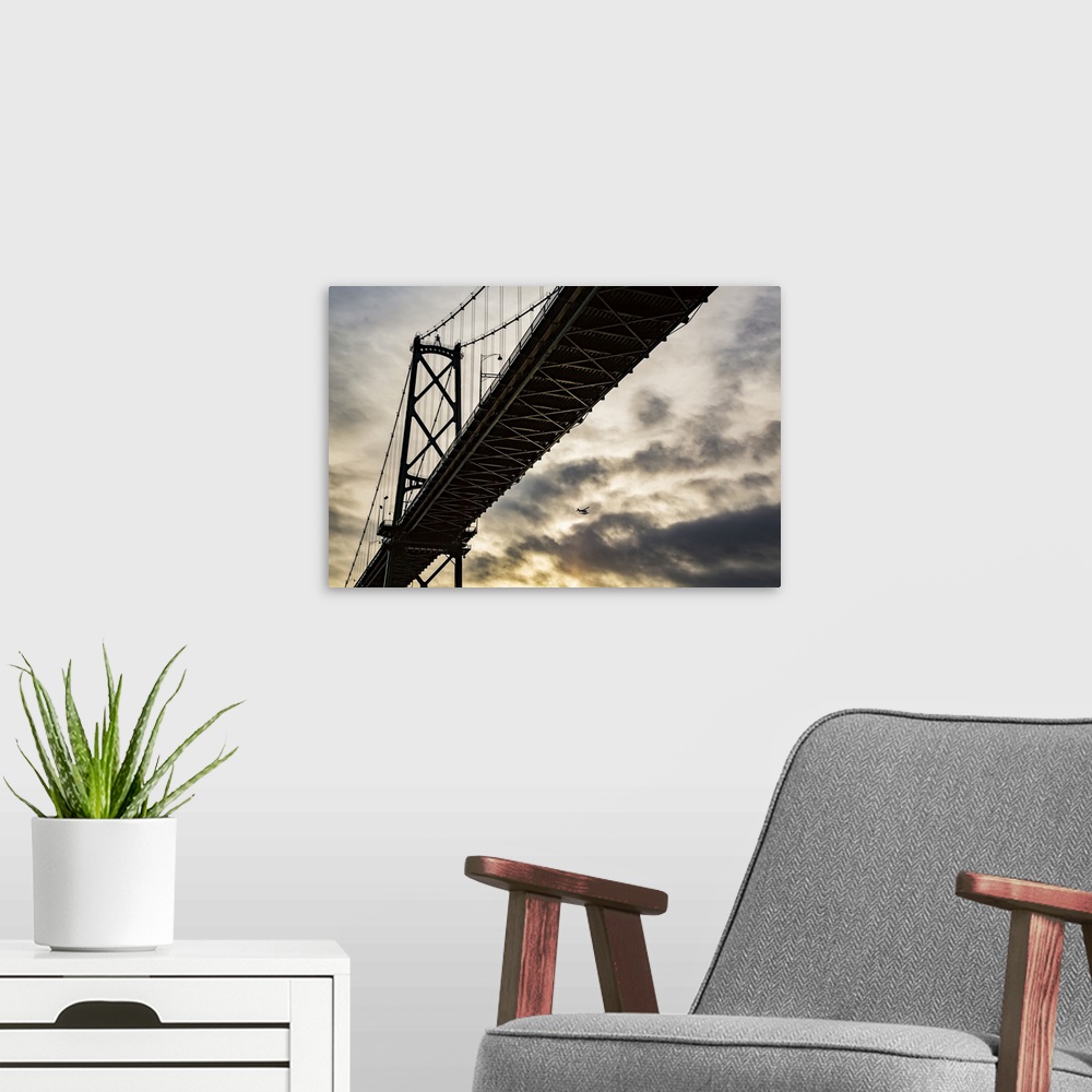 A modern room featuring Low angle view of a bridge at sunset with an airplane flying in the distance; Vancouver, British ...
